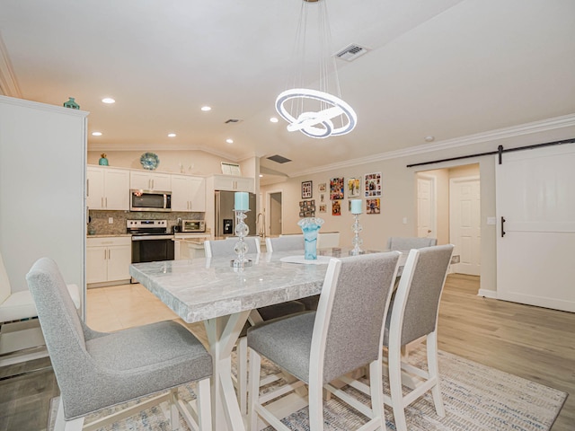 dining space with light wood-type flooring, a barn door, ornamental molding, and vaulted ceiling