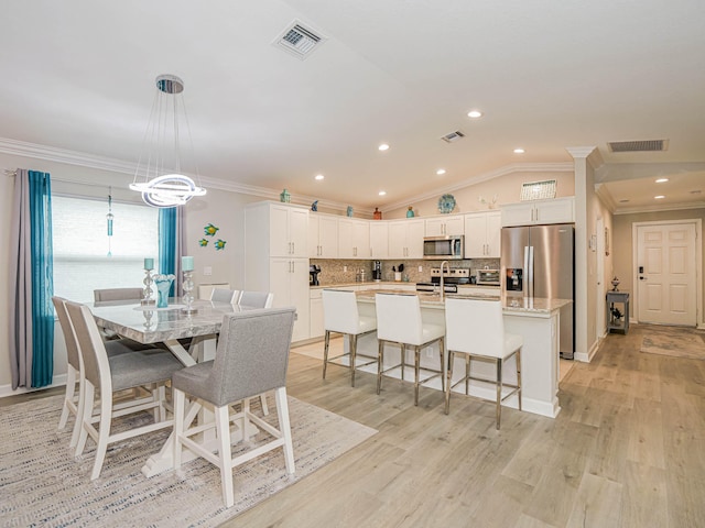 dining space with decorative columns, light hardwood / wood-style flooring, vaulted ceiling, and ornamental molding