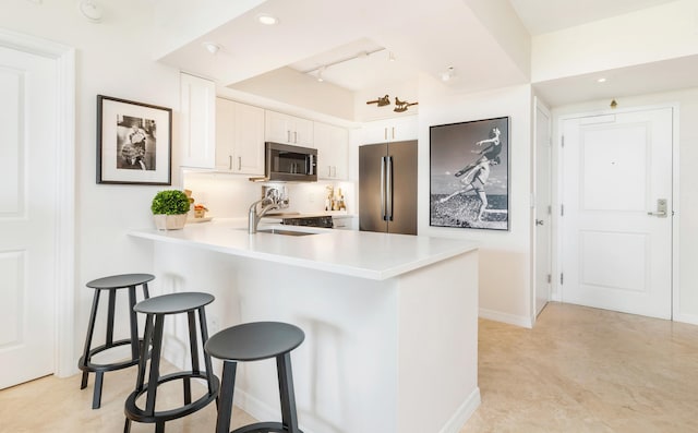 kitchen with kitchen peninsula, appliances with stainless steel finishes, a breakfast bar, sink, and white cabinetry