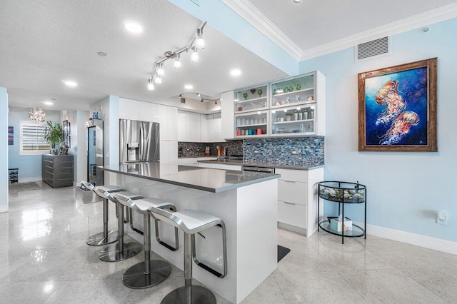 kitchen with a textured ceiling, stainless steel appliances, white cabinets, crown molding, and tasteful backsplash