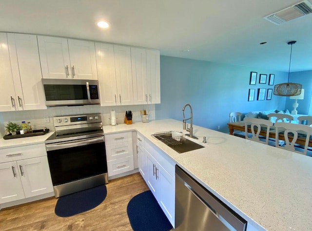 kitchen featuring appliances with stainless steel finishes, light hardwood / wood-style flooring, sink, and pendant lighting