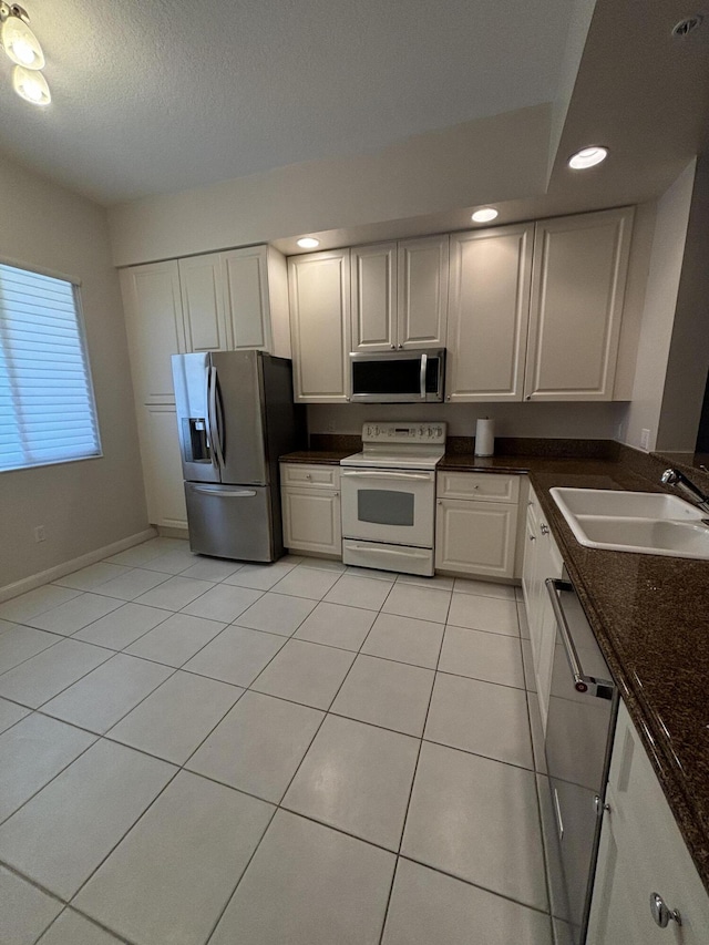 kitchen with dark stone countertops, light tile patterned floors, appliances with stainless steel finishes, white cabinets, and sink