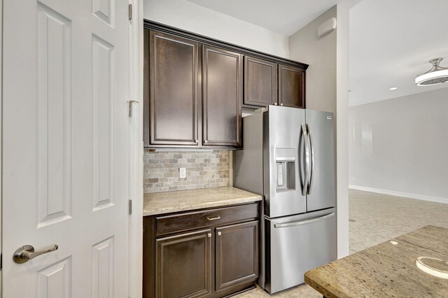 kitchen with stainless steel fridge with ice dispenser, decorative backsplash, dark brown cabinetry, light stone countertops, and baseboards