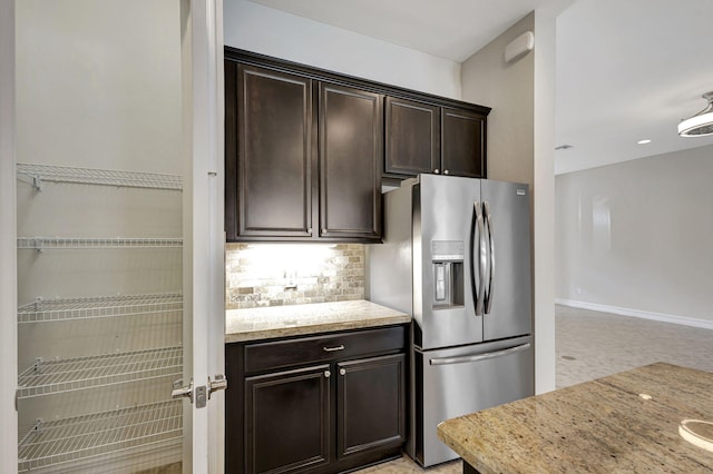 kitchen with dark brown cabinetry, baseboards, decorative backsplash, light stone countertops, and stainless steel refrigerator with ice dispenser