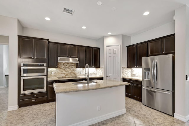 2710 W Mallory Blvd, Jupiter, FL 33458 - kitchen with stainless steel appliances, a sink, dark brown cabinetry, light stone counters, and a center island with sink