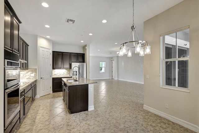 kitchen with tasteful backsplash, visible vents, a kitchen island with sink, dark brown cabinets, and baseboards