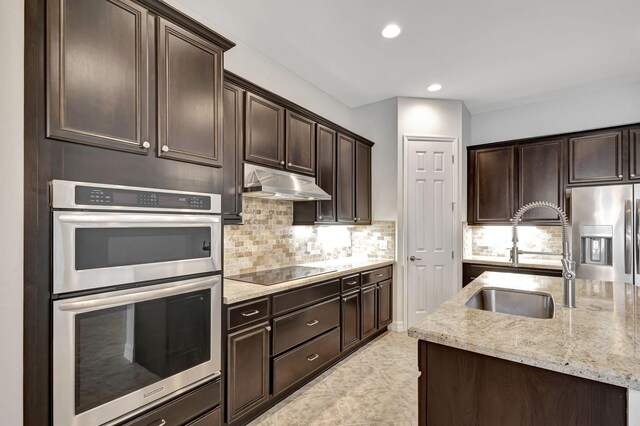 kitchen featuring dark brown cabinetry, sink, tasteful backsplash, appliances with stainless steel finishes, and light stone countertops