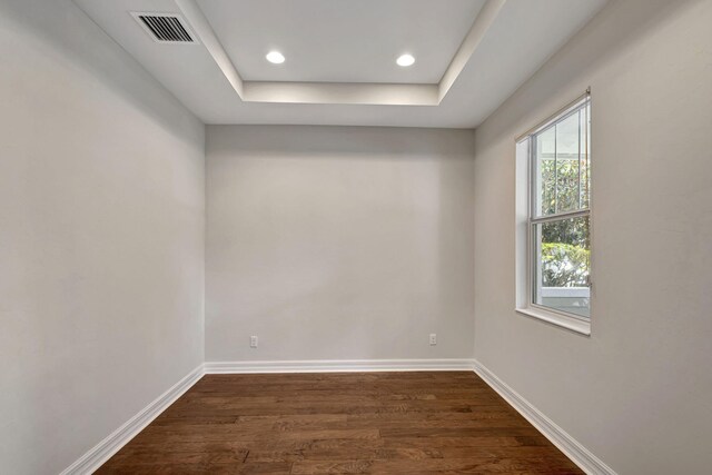 spare room with a tray ceiling and dark wood-type flooring