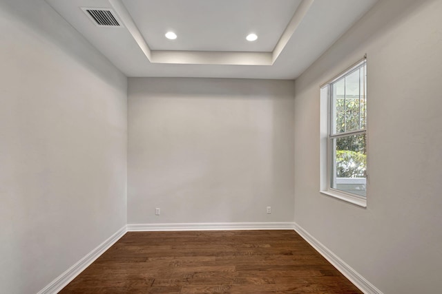 unfurnished room featuring dark wood-style floors, a tray ceiling, visible vents, and baseboards