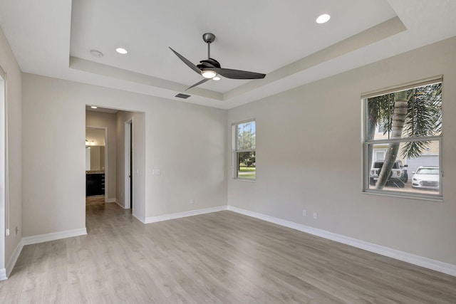 empty room with light wood finished floors, recessed lighting, a raised ceiling, ceiling fan, and baseboards