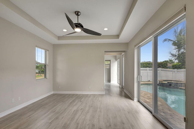 unfurnished room featuring a tray ceiling, ceiling fan, and light hardwood / wood-style flooring