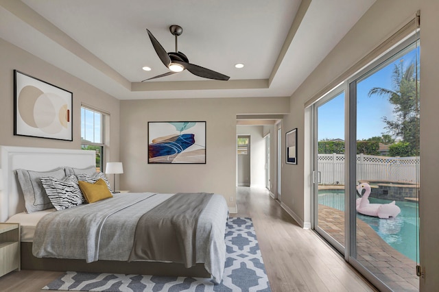 bedroom with ceiling fan, a tray ceiling, access to exterior, and light hardwood / wood-style flooring