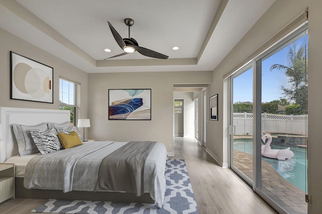 bedroom with access to outside, a raised ceiling, light wood-style flooring, and baseboards