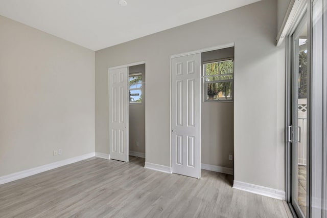 unfurnished bedroom featuring multiple windows, light wood-type flooring, and baseboards