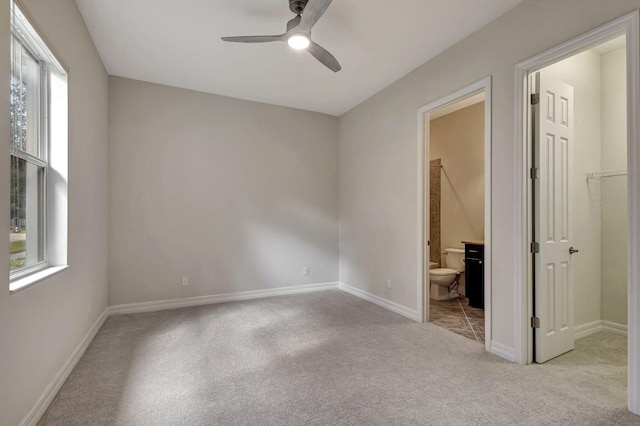 unfurnished bedroom with light colored carpet, a ceiling fan, baseboards, a walk in closet, and ensuite bath