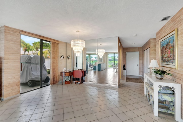 tiled entrance foyer with an inviting chandelier, wooden walls, and a textured ceiling