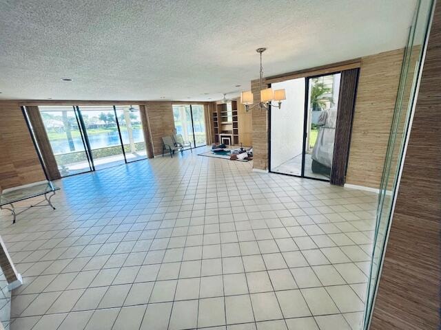 unfurnished dining area featuring light tile patterned floors, a textured ceiling, wood walls, and a chandelier