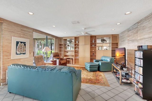 tiled living room with ceiling fan, a textured ceiling, and wood walls