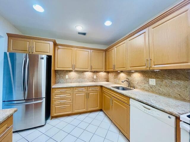 kitchen with sink, stainless steel refrigerator, decorative backsplash, light tile patterned floors, and white dishwasher