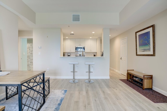 1203 Town Center Dr Unit 313, Jupiter, FL 33458 - kitchen featuring visible vents, light wood-style flooring, stainless steel microwave, tasteful backsplash, and white cabinetry