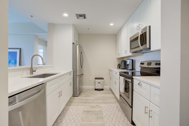 kitchen featuring appliances with stainless steel finishes, light hardwood / wood-style floors, white cabinetry, sink, and decorative backsplash