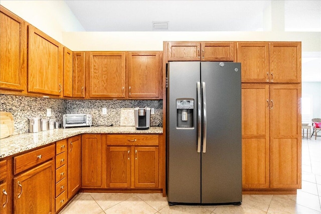 kitchen with decorative backsplash, stainless steel fridge, light tile patterned floors, and light stone countertops