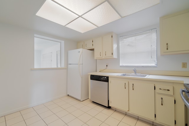 kitchen featuring cream cabinets, stainless steel dishwasher, light tile patterned floors, white fridge, and sink