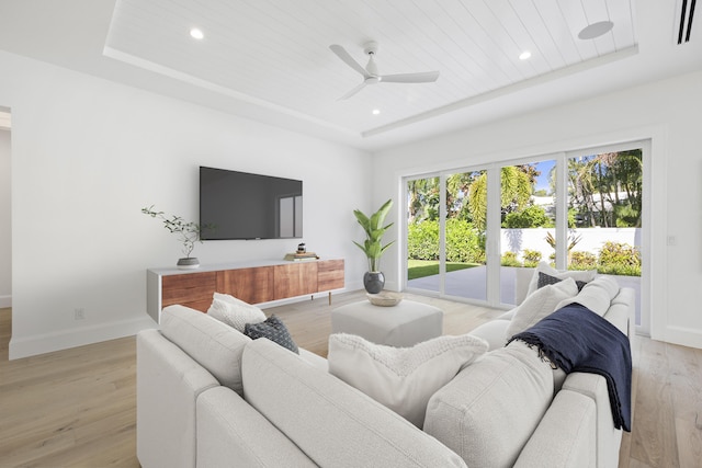 living room with a tray ceiling, ceiling fan, and light hardwood / wood-style floors