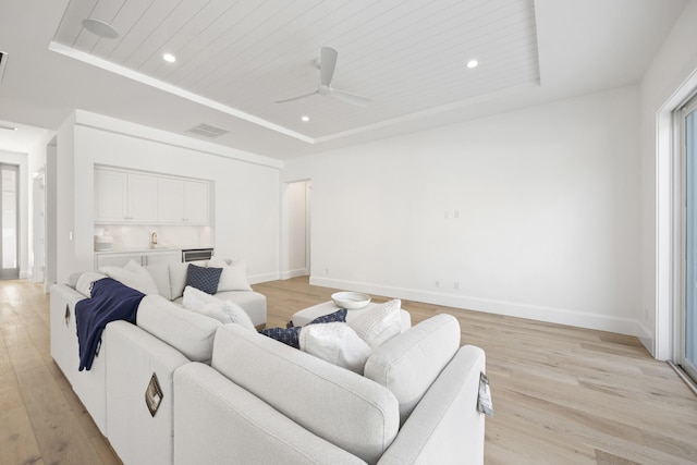 living room with a raised ceiling, ceiling fan, sink, and light hardwood / wood-style flooring