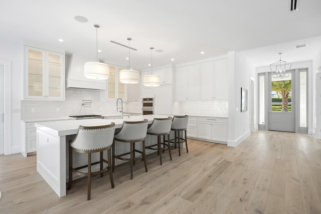 kitchen featuring light wood-type flooring, white cabinetry, pendant lighting, a kitchen bar, and a kitchen island with sink