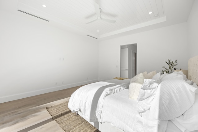 bedroom with light wood-type flooring, a tray ceiling, and ceiling fan