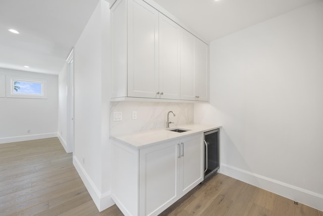 bar featuring white cabinetry, beverage cooler, sink, decorative backsplash, and light hardwood / wood-style floors