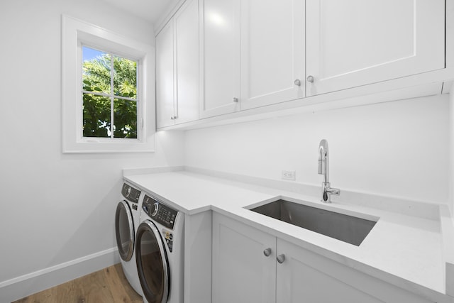 laundry room featuring hardwood / wood-style flooring, washing machine and clothes dryer, cabinets, and sink