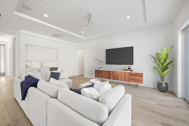 living room with ceiling fan, a raised ceiling, and light hardwood / wood-style flooring