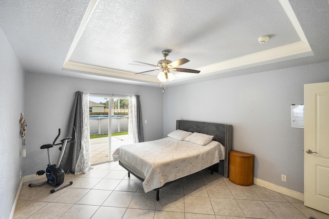 tiled bedroom featuring a textured ceiling, ceiling fan, access to exterior, and a tray ceiling