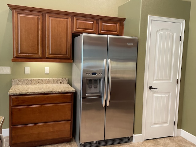 kitchen with brown cabinets, stainless steel fridge, baseboards, and light stone countertops