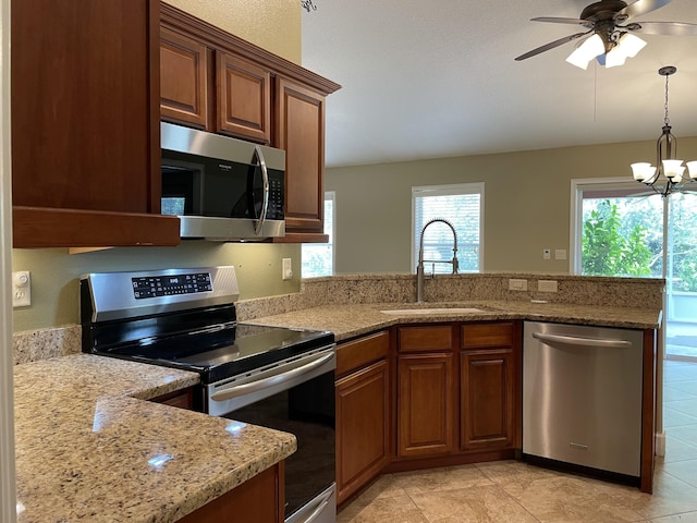 kitchen with appliances with stainless steel finishes, brown cabinetry, a sink, and light stone countertops