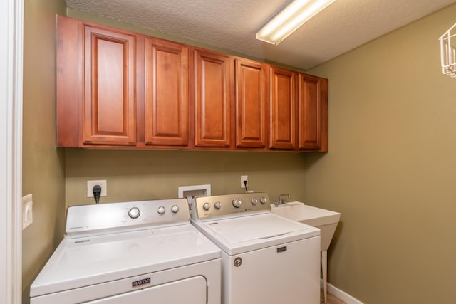 clothes washing area featuring a textured ceiling, independent washer and dryer, cabinet space, and baseboards