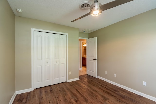 unfurnished bedroom featuring a textured ceiling, visible vents, baseboards, a closet, and dark wood-style floors