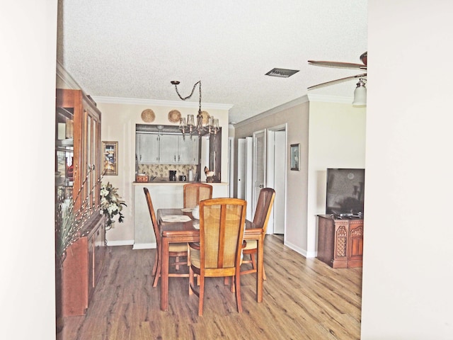 dining room featuring a textured ceiling, hardwood / wood-style flooring, ornamental molding, and ceiling fan with notable chandelier