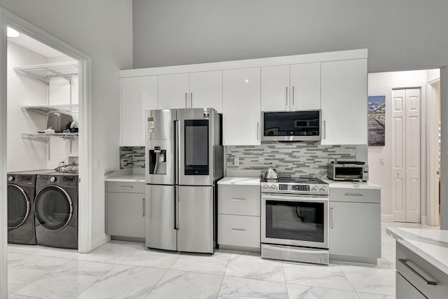 kitchen with gray cabinets, light tile patterned flooring, stainless steel appliances, backsplash, and washing machine and clothes dryer