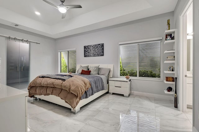 bedroom featuring ensuite bath, a barn door, light tile patterned floors, ceiling fan, and a raised ceiling