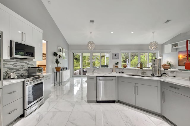 kitchen featuring appliances with stainless steel finishes, hanging light fixtures, backsplash, light tile patterned floors, and vaulted ceiling