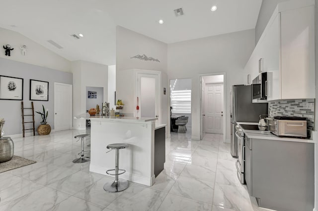 kitchen featuring stainless steel appliances, a kitchen breakfast bar, vaulted ceiling, light tile patterned flooring, and tasteful backsplash