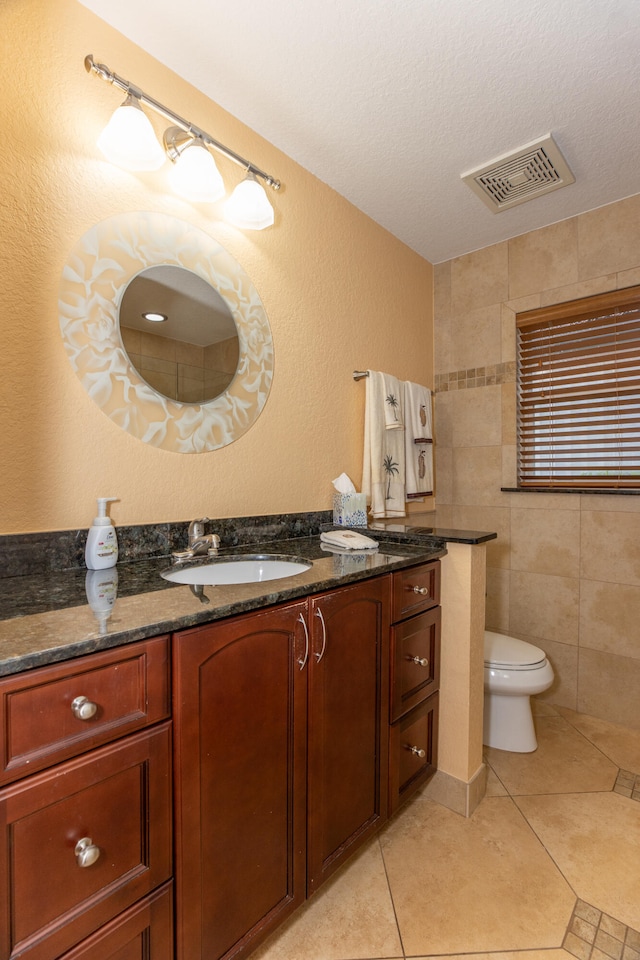 bathroom with a textured ceiling, toilet, tile walls, tile patterned floors, and vanity