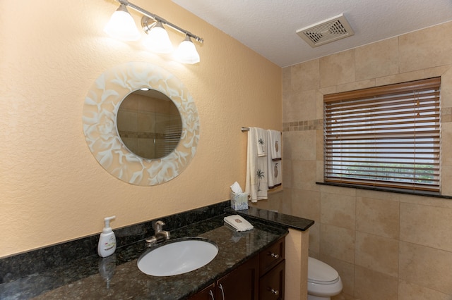 bathroom featuring tile walls, a textured ceiling, toilet, and vanity