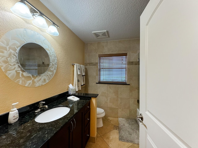 bathroom featuring a textured ceiling, toilet, tile patterned floors, tile walls, and vanity