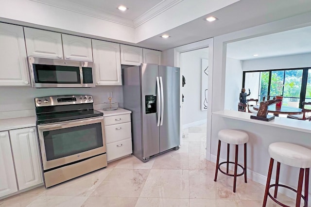 kitchen with a breakfast bar area, stainless steel appliances, white cabinetry, light countertops, and ornamental molding