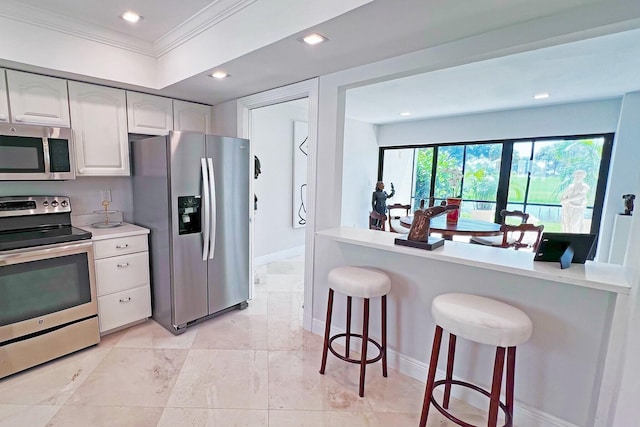 kitchen with light countertops, appliances with stainless steel finishes, ornamental molding, white cabinetry, and a kitchen bar