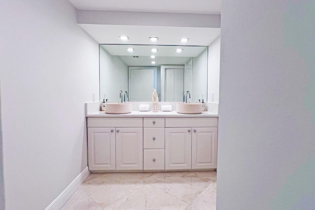 bathroom featuring double vanity, marble finish floor, baseboards, and a sink